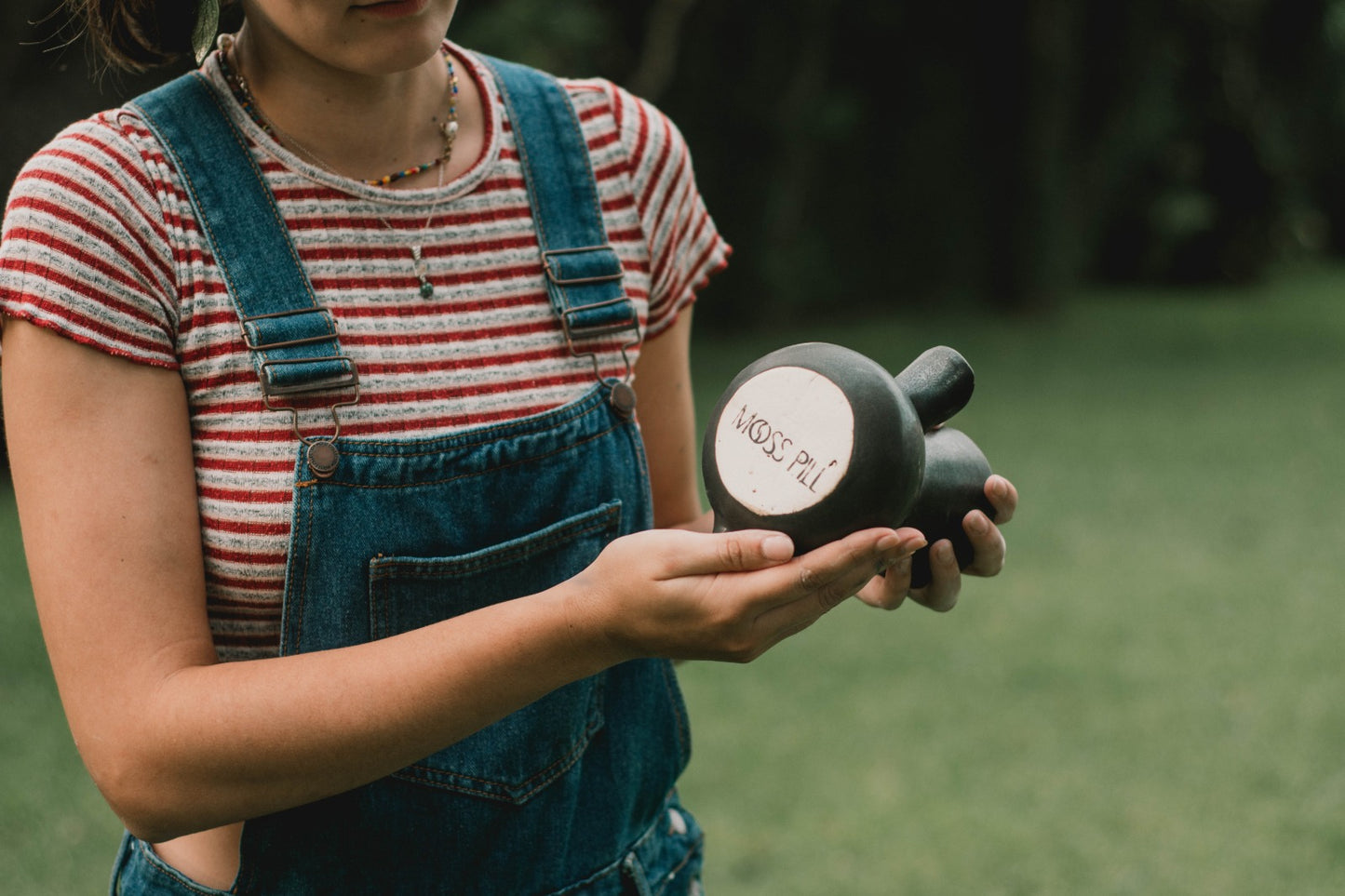 The Kápi Coffee Maker, a handcrafted clay pot from Costa Rica, with a matte black finish. Its elegant, simple design features a flared top, sturdy handle, and a distinctive oxygenation hole for enhancing the coffee's flavor. The artisanal craftsmanship is evident in the pot's textured surface and organic shape, embodying a blend of tradition and functionality in its compact form.